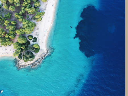 Aerial view of bright turqoise water and beach with pine forest.