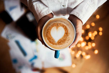 girl holding a coffee cup with a heart with a work backgroundの写真素材