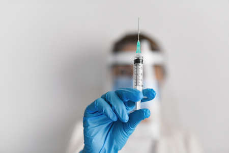 Female doctor wearing protective equipment with a syringe - covid-19 health concept
