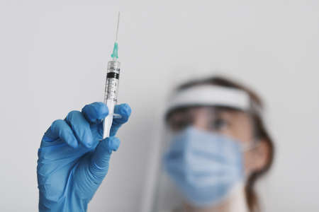 Female doctor wearing protective equipment with a syringe - covid-19 health conceptの写真素材