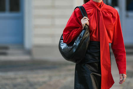 Milan, Italy - September 24, 2021:  Street style outfit, fashionable woman wearing  a red oversized wrap shirt with a knotted neck, a black shiny leather shoulder bag, a black shiny leather high waist knees skirt on the streets of Milan, Italy.のeditorial素材