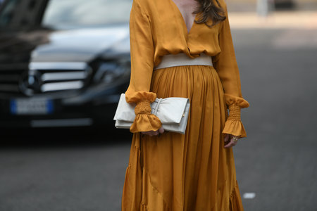 Milan, Italy - September 22, 2021:  Street style outfit, woman wearinga leather belt, a long yellow mustard dress, a white clutch and block heels sandals on the streets of Milan, Italy.のeditorial素材