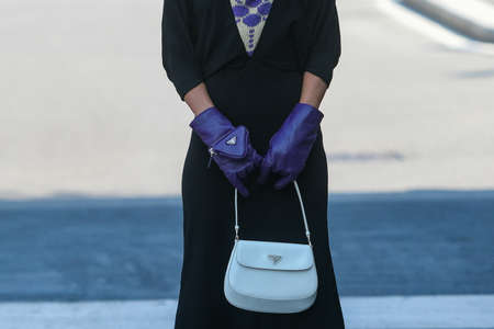 Milan, Italy - September 24, 2021:  Street style outfit, fashionable woman wearing a long Prada black dress, purple gloves, Prada earings and white Prada bag on the streets of Milan, Italy.のeditorial素材