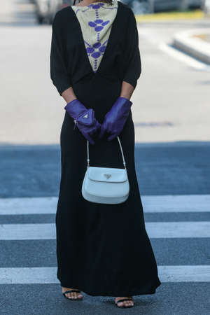 Milan, Italy - September 24, 2021:  Street style outfit, fashionable woman wearing a long Prada black dress, purple gloves, Prada earings and white Prada bag on the streets of Milan, Italy.のeditorial素材