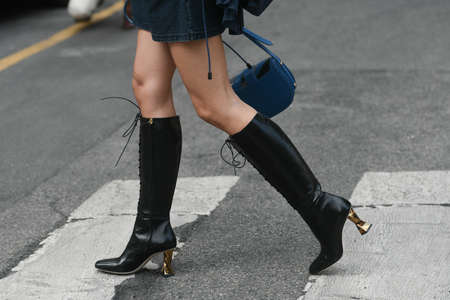 Milan, Italy - September 22, 2021:  Street style outfit, woman wearinga blue and gray bag with black pattern and black shiny leather boots with gold block heels on the streets of Milan, Italy.のeditorial素材