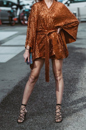 Milan, Italy - February, 24: Street style, woman wearing orange belted short dress and black shiny...