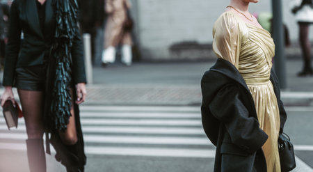 Milan, Italy - February, 24: Street style, woman wearing yellow shiny satin transparent dress, a black long coat, a black grained leather handbag and black ankle boots.のeditorial素材