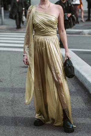 Milan, Italy - February, 24: Street style, woman wearing yellow shiny satin transparent dress, a black long coat, a black grained leather handbag and black ankle boots.のeditorial素材