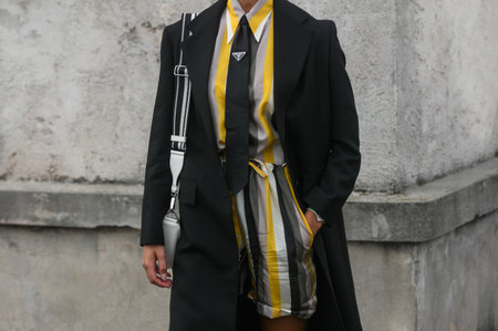 Milan, Italy - February, 24: Street style, woman wearing yellow and grey shirt with matching shorts, black Prada tie, black coat, white Prada bag.のeditorial素材