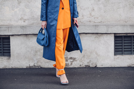 Milan, Italy - February, 24: Street style, woman wearing yellow shiny satin transparent dress, a black long coat, a black grained leather handbag and black ankle boots.のeditorial素材
