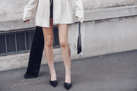 Milan, Italy - February, 24: Street style, woman wearing yellow shiny satin transparent dress, a black long coat, a black grained leather handbag and black ankle boots.のeditorial素材