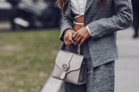 Milan, Italy - February, 24: Street style, woman wearing white cropped shirt, a gray blazer jacket, gray matching suit pants, a beige leather handbag and yellow green open toe-cap pumps sandals.のeditorial素材