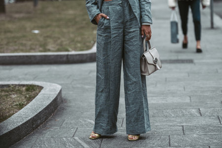 Milan, Italy - February, 24: Street style, woman wearing white cropped shirt, a gray blazer jacket, gray matching suit pants, a beige leather handbag and yellow green open toe-cap pumps sandals.のeditorial素材