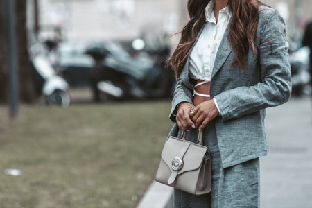 Milan, Italy - February, 24: Street style, woman wearing white cropped shirt, a gray blazer jacket, gray matching suit pants, a beige leather handbag and yellow green open toe-cap pumps sandals.のeditorial素材