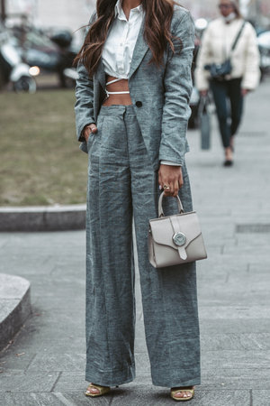Milan, Italy - February, 24: Street style, woman wearing white cropped shirt, a gray blazer jacket, gray matching suit pants, a beige leather handbag and yellow green open toe-cap pumps sandals.のeditorial素材