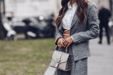 Milan, Italy - February, 24: Street style, woman wearing white cropped shirt, a gray blazer jacket, gray matching suit pants, a beige leather handbag and yellow green open toe-cap pumps sandals.のeditorial素材