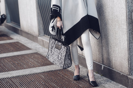 Milan, Italy - February 25, 2022: Crop anonymous female in trendy outfit with ornamental pattern on Etro handbag standing near concrete wall.のeditorial素材