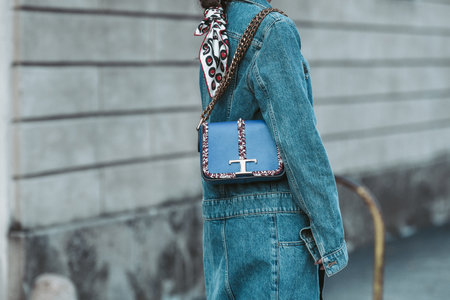 Milan, Italy - February 25, 2022: Crop anonymous female in denim outfit with blue Tod's handbag with chain walking on street.のeditorial素材