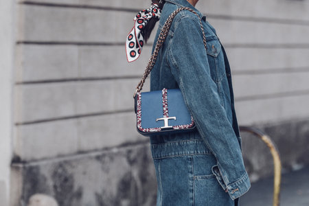 Milan, Italy - February 25, 2022: Crop anonymous female in denim outfit with blue Tod's handbag with chain walking on street.のeditorial素材