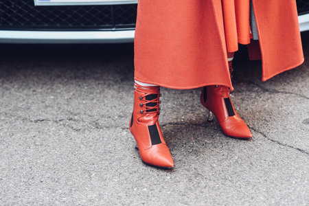 Milan, Italy - February 25, 2022: Woman in extravagant red high heeled boots and coat standing.のeditorial素材
