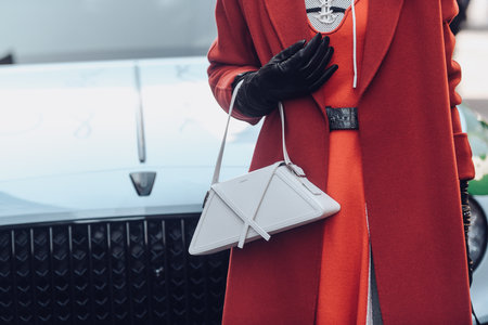 Milan, Italy - February 25, 2022: Woman in elegant vivid red coat and leather black gloves holding white bag.のeditorial素材