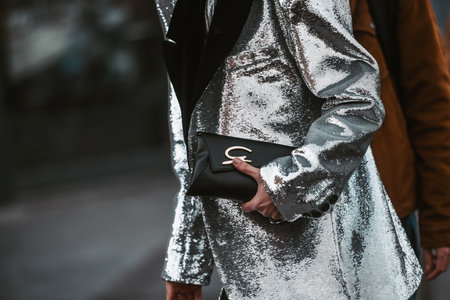 Milan, Italy - February 24, 2022: Crop anonymous trendy person in silver jacket with black handbag walking on street in Milanのeditorial素材