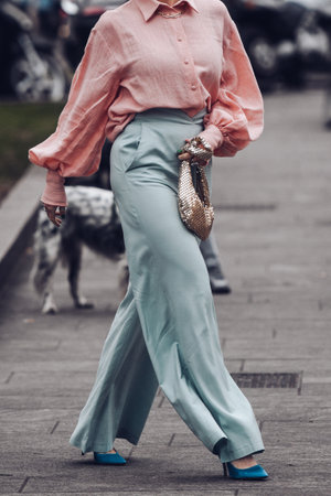 Milan, Italy - February 24, 2022: Woman in pink long coat green pants and blue high heeled shoes with golden handbag.のeditorial素材