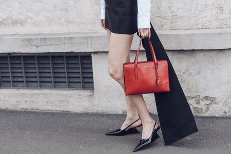 Milan, Italy - February 24, 2022: Woman in black dress with white sleeves wearing unusual pointy toe shoes walking on street with red handbag.のeditorial素材