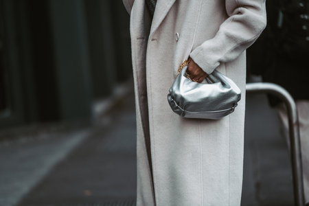 Milan, Italy - February 24, 2022: Female in beige long coat with silver handbag.のeditorial素材