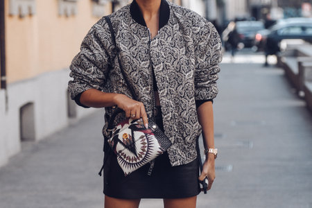 Milan, Italy - February 25, 2022: Female wearing an ornamental silver blazer, black leather skirt and white pattern handbag.のeditorial素材