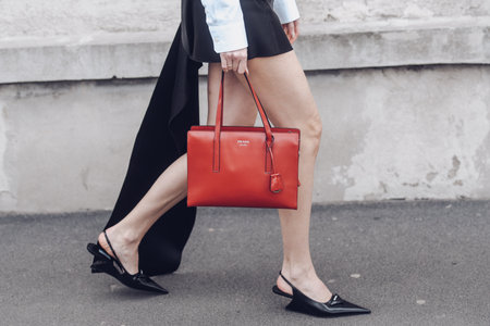 Milan, Italy - February 24, 2022: Woman in black dress with white sleeves wearing unusual pointy toe shoes walking on street with red handbag.のeditorial素材