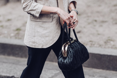 Milan, Italy - February 24, 2022: Woman in beige jacket tie and black trousers standing with handbag.のeditorial素材