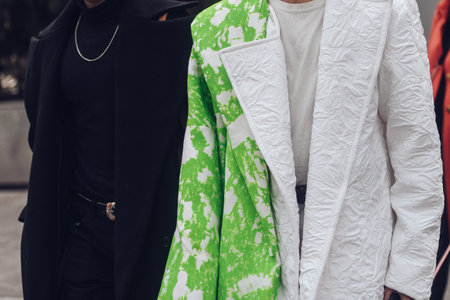 Milan, Italy - February 24, 2022: Woman in black coat turtleneck and pants with necklace walking on street with friend in white textured jacket with light green printのeditorial素材