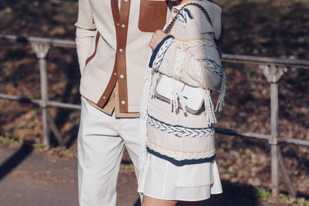 Milan, Italy - February 24, 2022: Man in beige trousers and quilted overshirt with brown leather pockets walking with female in skirt and knitted sweater with horizontal lines.のeditorial素材
