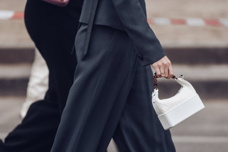 Milan, Italy - February 24, 2022: crop unrecognizable woman in black suit with white handbag.のeditorial素材