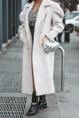 Milan, Italy - February 24, 2022: Female in beige long coat with silver handbag.のeditorial素材