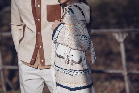 Milan, Italy - February 24, 2022: Man in beige trousers and quilted overshirt with brown leather pockets walking with female in skirt and knitted sweater with horizontal lines.のeditorial素材