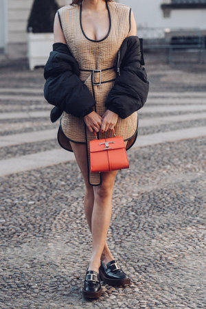 Milan, Italy - February 24, 2022: Woman wearing brown short belted dress and black jacket standing with orange handbag.のeditorial素材