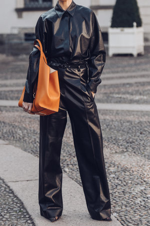 Milan, Italy - February 24, 2022: Woman in black leather jumpsuit standing with hand in pocket and orange bag.のeditorial素材