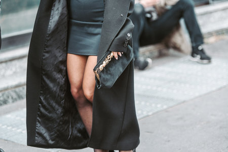 Milan, Italy - February 24, 2022: Woman in long black coat and short tight dress with handbag.のeditorial素材