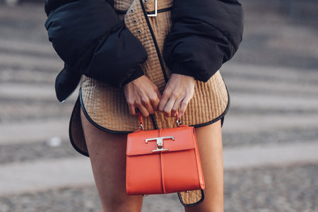 Milan, Italy - February 24, 2022: Woman wearing brown short belted dress and black jacket standing with orange handbag.のeditorial素材