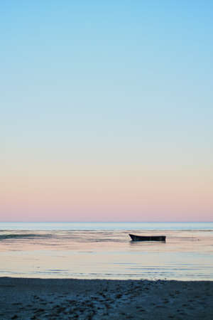 Small fishing boat in bay at dusk sunsetの写真素材