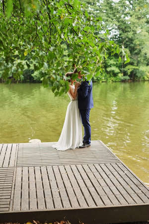 Beautiful wedding couple, bride,groom kissing and posing on the pirse near lakeの写真素材