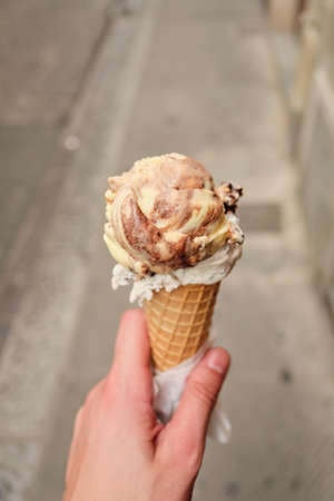 A first person view, a person walking along the road with an chocolatte ice cream in his hands, shallow depth of field.の写真素材