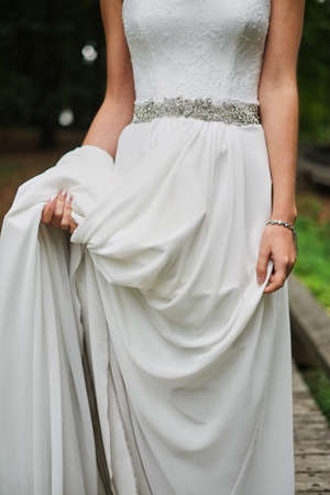 Bride in an elegant silk dress stands and holds the dress by the edge beltの写真素材