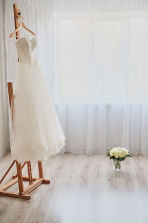 Beautiful wedding dress on a hanger in the room light backgroundの写真素材