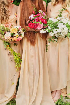 Three bridesmaids in gently orange dresses hold wedding bouquetsの写真素材