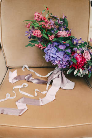 Wedding bouquet with purple and blue flowers, greens and ribbons on the chairの写真素材