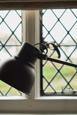 black table lamp in the interior against the window with rhombuses. Business or education concept with place for your text. Fragment of interior, minimalism background.の写真素材