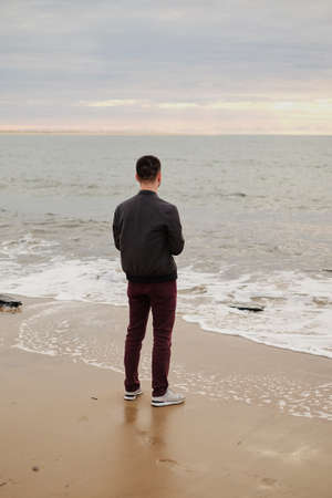 a handsome young guy on the background of the sea stands in the wind and gazes into the distance